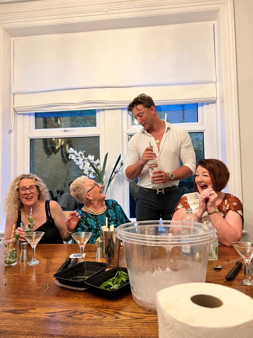 Our bartender shaking a cocktail while two guests laugh beside him